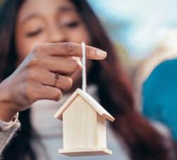 Mulher segura miniatura de uma casa em seus dedos e se pergunta o que é hipoteca de imóvel
