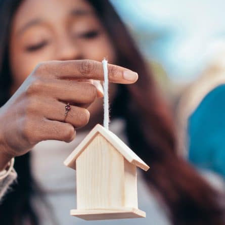 Mulher segura miniatura de uma casa em seus dedos e se pergunta o que é hipoteca de imóvel