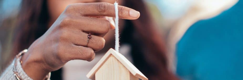 Mulher segura miniatura de uma casa em seus dedos e se pergunta o que é hipoteca de imóvel