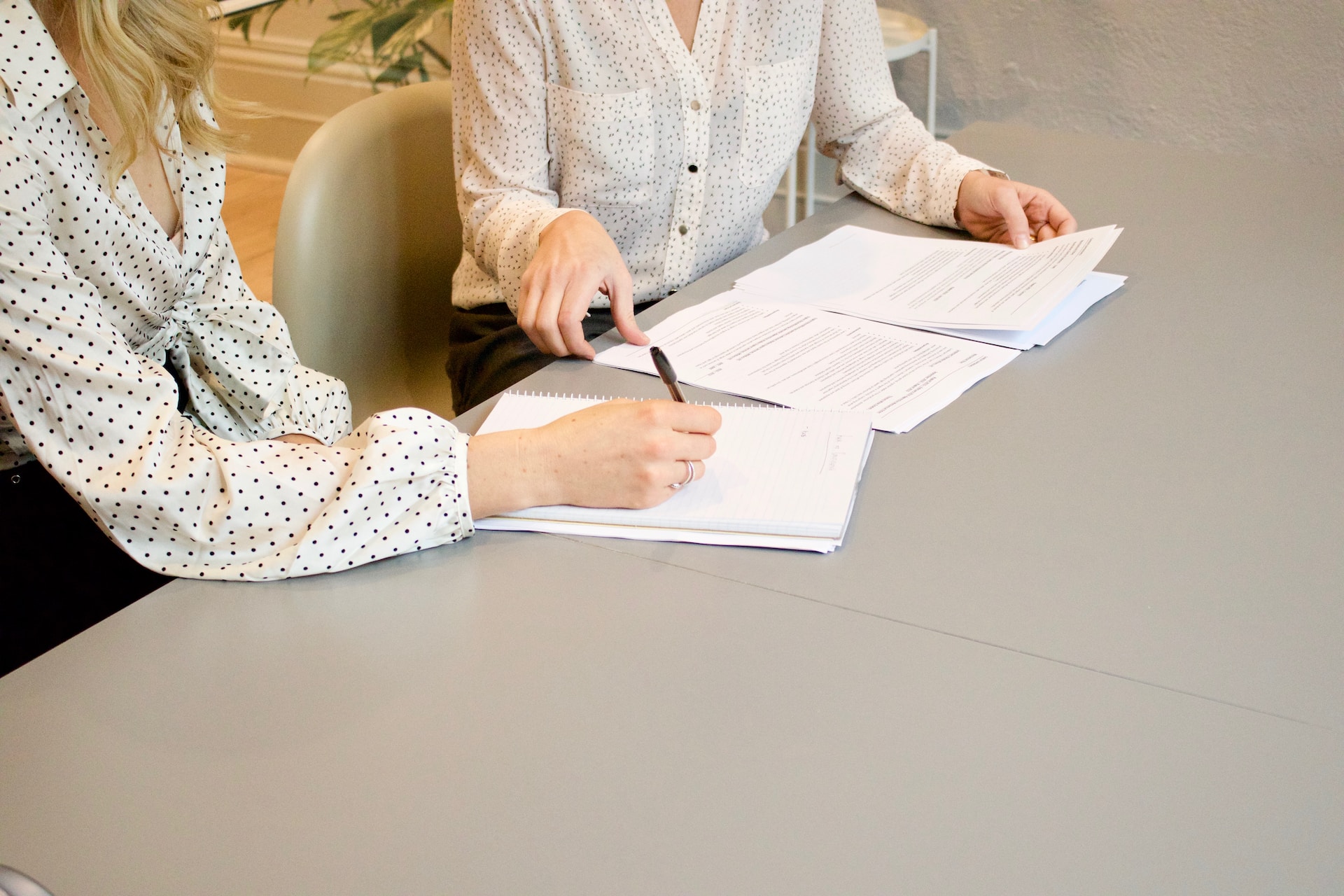 Duas mulheres sentadas em uma mesa assinando e conferindo um aditivo de contrato