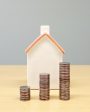 Casa em miniatura ao fundo com três pilhas de moedas em crescimento à frente, representando valorização e investimento em fundos imobiliários.